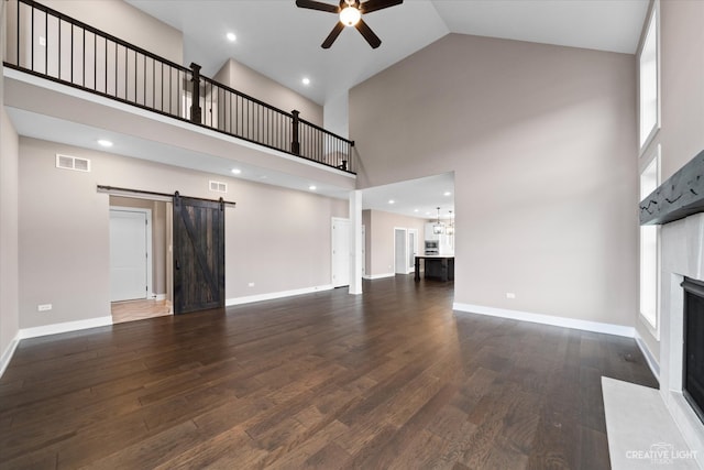 unfurnished living room featuring a barn door, dark hardwood / wood-style floors, and high vaulted ceiling