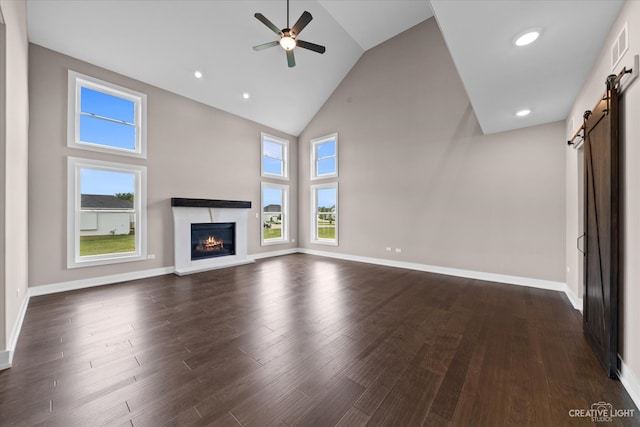 unfurnished living room with high vaulted ceiling, dark hardwood / wood-style floors, plenty of natural light, and a barn door