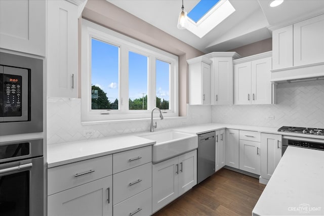 kitchen featuring white cabinets, vaulted ceiling with skylight, sink, appliances with stainless steel finishes, and dark hardwood / wood-style floors