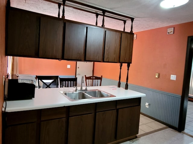 kitchen featuring dark brown cabinets, light tile patterned flooring, sink, and kitchen peninsula