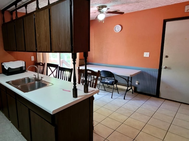 kitchen featuring dark brown cabinetry, ceiling fan, light tile patterned floors, sink, and a textured ceiling