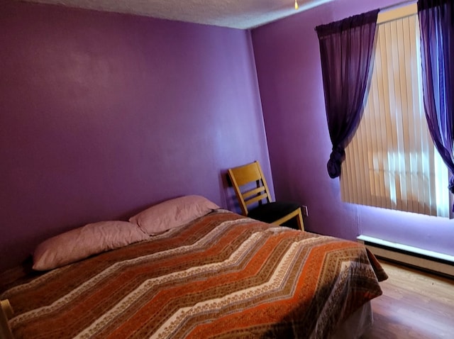 bedroom with wood-type flooring, a textured ceiling, and a baseboard radiator