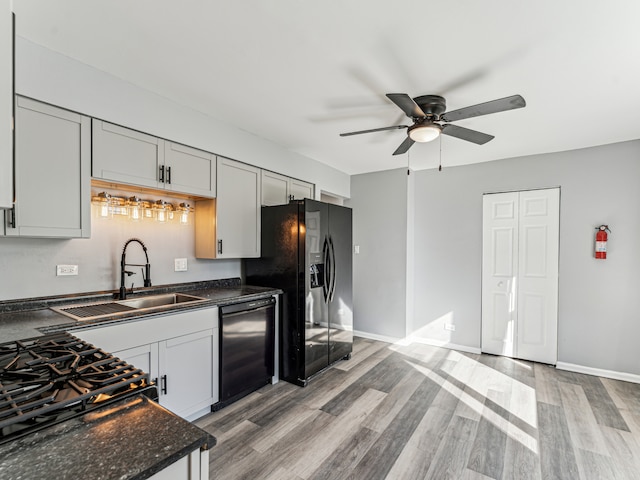 kitchen with black appliances, sink, light hardwood / wood-style floors, ceiling fan, and dark stone counters