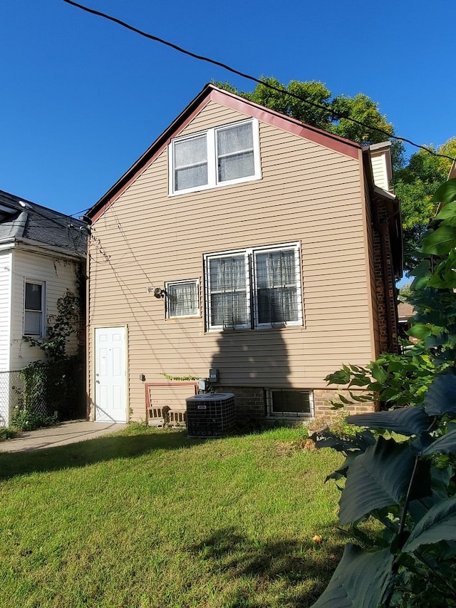 rear view of house with central AC unit and a yard