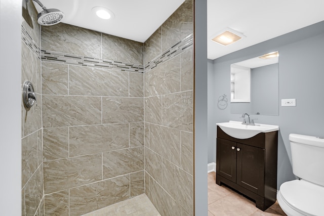 bathroom featuring tile patterned flooring, a tile shower, vanity, and toilet