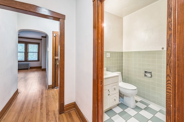 bathroom featuring radiator heating unit, hardwood / wood-style flooring, tile walls, toilet, and vanity