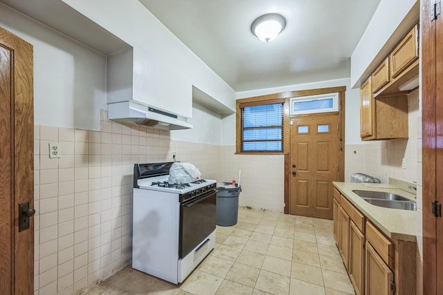 kitchen with white gas range, range hood, sink, light tile patterned floors, and tile walls