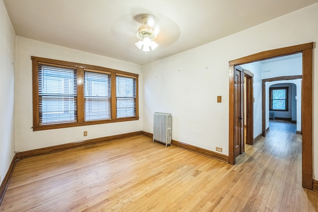 empty room with ceiling fan, light wood-type flooring, and radiator