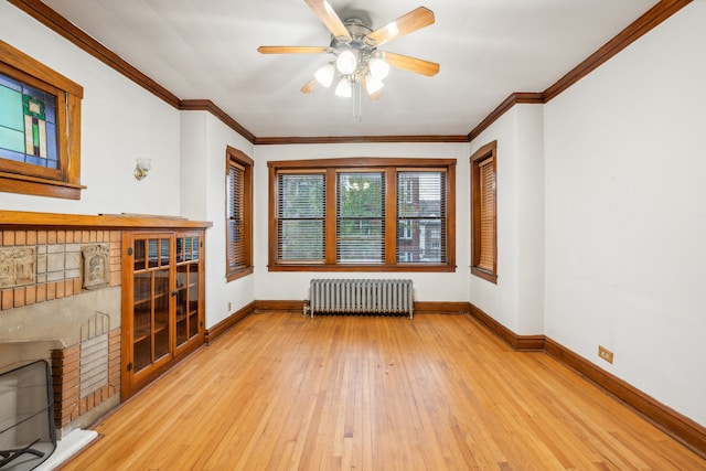 unfurnished living room with radiator heating unit, a brick fireplace, light hardwood / wood-style floors, ceiling fan, and ornamental molding