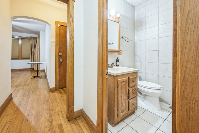 bathroom featuring vanity, toilet, wood-type flooring, and tile walls