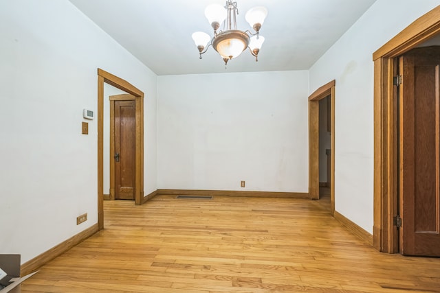 spare room with an inviting chandelier and light wood-type flooring