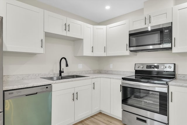 kitchen featuring appliances with stainless steel finishes, light wood-type flooring, sink, and white cabinetry