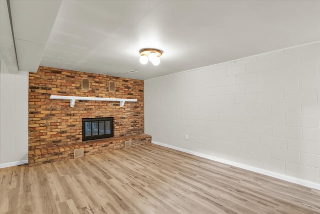 unfurnished living room with light wood-type flooring, brick wall, and a brick fireplace