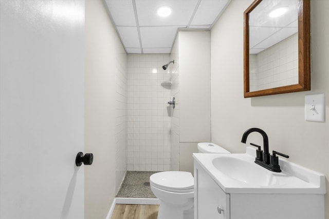 bathroom featuring wood-type flooring, tiled shower, vanity, and toilet