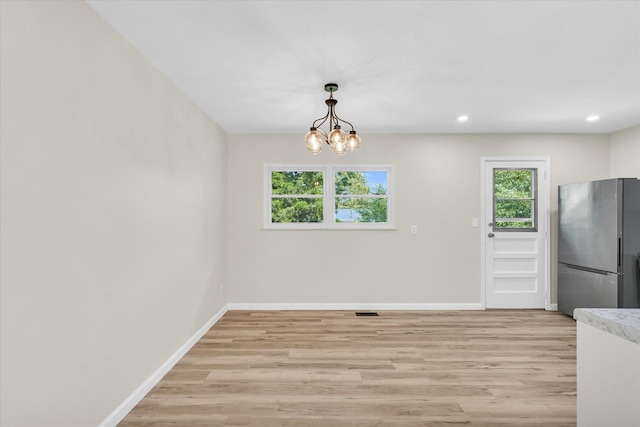 unfurnished dining area with light wood-type flooring and a chandelier