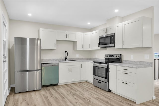 kitchen with stainless steel appliances, white cabinetry, light hardwood / wood-style floors, and sink