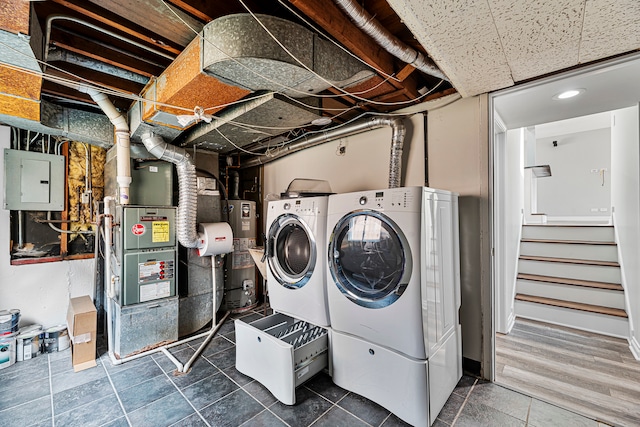 laundry area featuring electric panel, heating unit, washing machine and dryer, tile patterned floors, and gas water heater