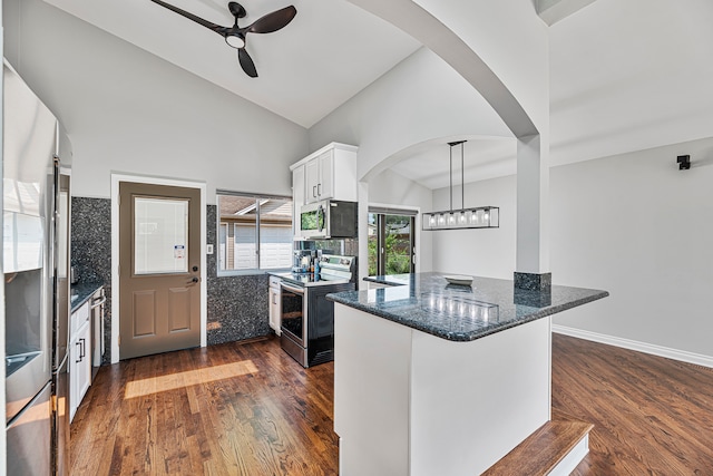 kitchen featuring dark stone counters, white cabinets, kitchen peninsula, appliances with stainless steel finishes, and dark hardwood / wood-style flooring