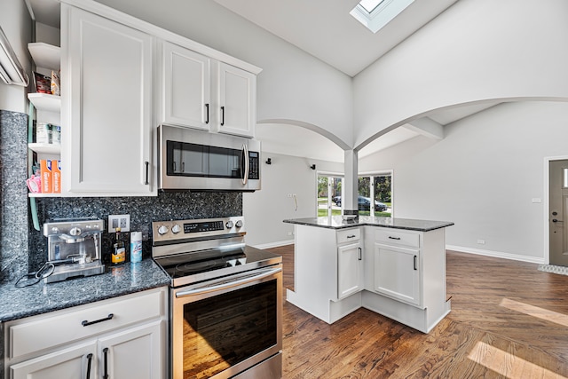 kitchen with white cabinets, high vaulted ceiling, backsplash, appliances with stainless steel finishes, and dark stone countertops