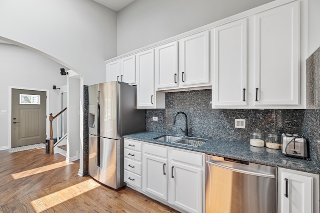 kitchen with white cabinets, sink, dark stone counters, stainless steel appliances, and light wood-type flooring