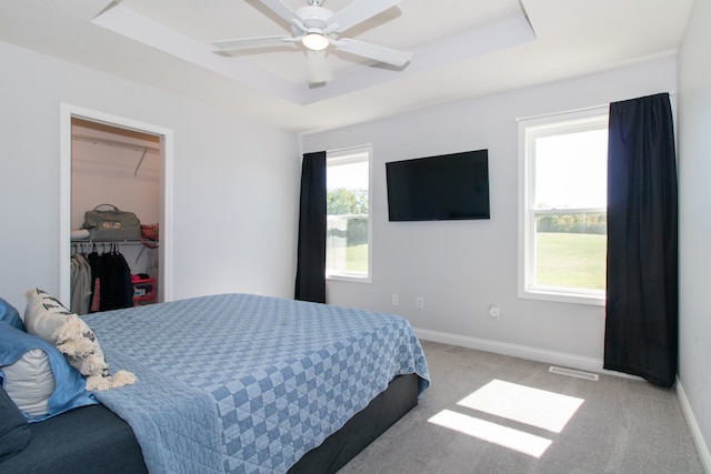 carpeted bedroom featuring multiple windows, a raised ceiling, ceiling fan, and a closet