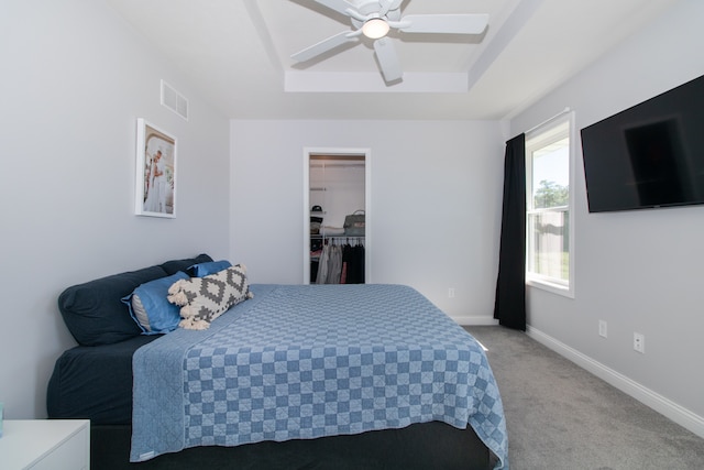 bedroom featuring ceiling fan, a raised ceiling, a walk in closet, a closet, and light colored carpet