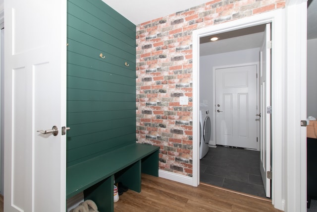 mudroom with washer / clothes dryer, dark wood-type flooring, and brick wall