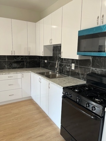 kitchen with sink, black range with gas cooktop, backsplash, white cabinetry, and light hardwood / wood-style floors