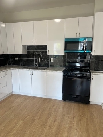 kitchen featuring white cabinetry, light hardwood / wood-style floors, black gas range oven, and sink