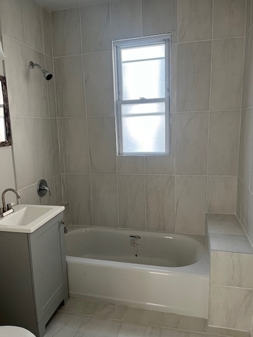 bathroom with tiled shower / bath combo, vanity, and tile walls