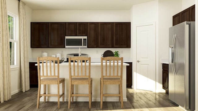 kitchen with appliances with stainless steel finishes, dark brown cabinetry, light hardwood / wood-style flooring, and a breakfast bar