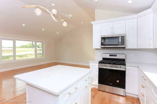 kitchen featuring hanging light fixtures, vaulted ceiling, white cabinetry, stainless steel appliances, and light wood-type flooring