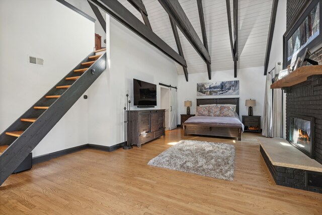 living room featuring light wood-type flooring, beam ceiling, a fireplace, a barn door, and high vaulted ceiling