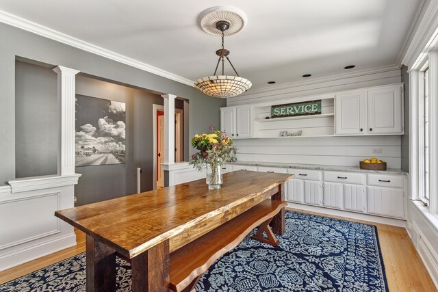 dining room with crown molding, decorative columns, and light hardwood / wood-style flooring