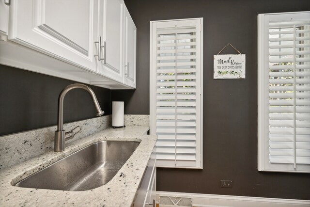 kitchen featuring light stone countertops, white cabinets, and sink