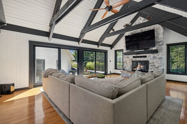 living room featuring a fireplace, wood walls, beam ceiling, ceiling fan, and light hardwood / wood-style flooring