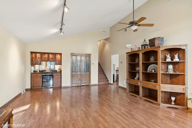 unfurnished living room with ceiling fan, wine cooler, high vaulted ceiling, rail lighting, and hardwood / wood-style flooring