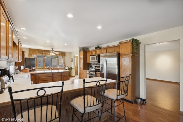 kitchen featuring stainless steel appliances, kitchen peninsula, dark wood-type flooring, and a kitchen breakfast bar