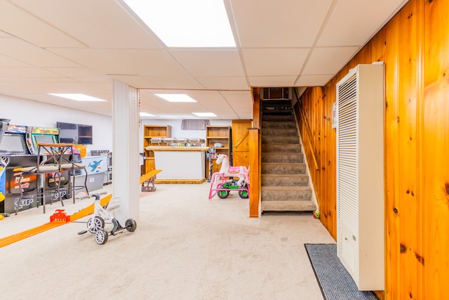 basement with wood walls, carpet flooring, and a paneled ceiling