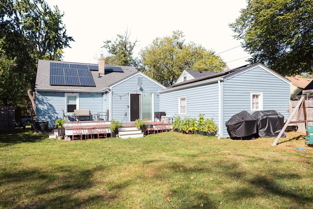 rear view of house with solar panels, a wooden deck, and a yard