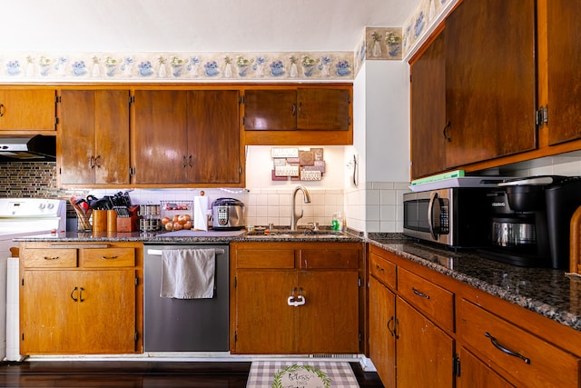 kitchen with dark stone countertops, backsplash, stainless steel appliances, range hood, and sink