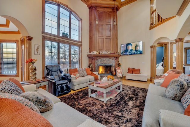 living room with wood-type flooring, a high ceiling, a large fireplace, crown molding, and ornate columns