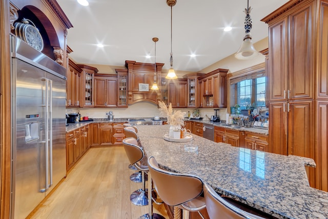 kitchen featuring a kitchen breakfast bar, stone countertops, pendant lighting, stainless steel appliances, and light hardwood / wood-style flooring