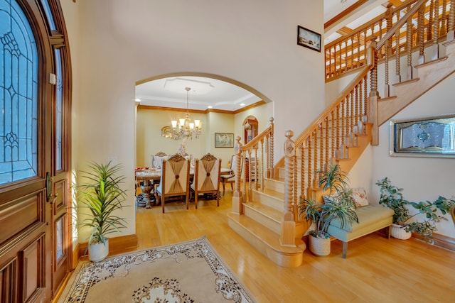 entrance foyer with a notable chandelier, light wood-type flooring, ornamental molding, and a high ceiling