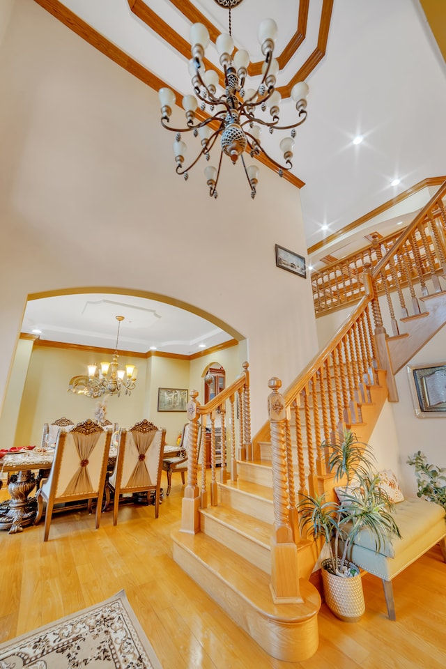 stairs featuring crown molding, a high ceiling, a chandelier, and hardwood / wood-style flooring