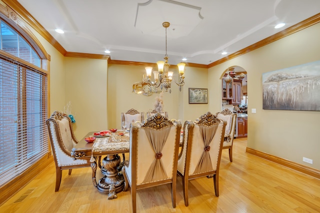 dining area with light wood-type flooring, crown molding, and a notable chandelier