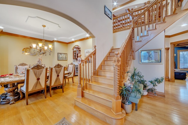 staircase featuring wood-type flooring, an inviting chandelier, and ornamental molding