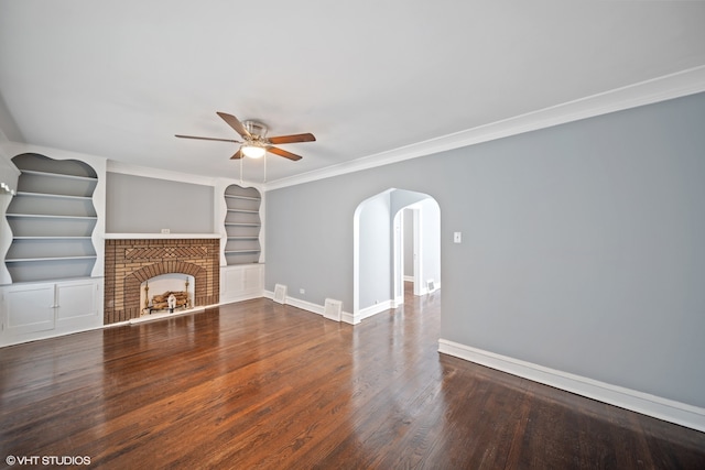 unfurnished living room featuring dark wood-type flooring, ornamental molding, a brick fireplace, built in features, and ceiling fan