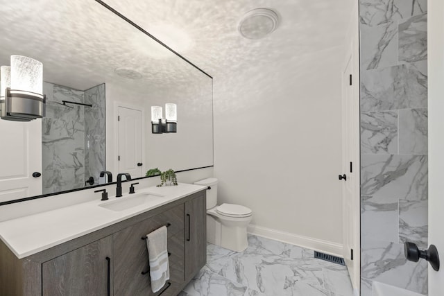 bathroom with a textured ceiling, toilet, vanity, and tiled shower