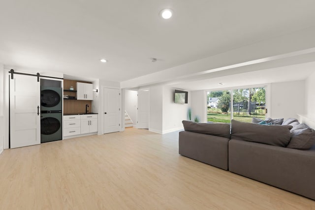 living room with stacked washer and clothes dryer, light hardwood / wood-style flooring, and a barn door